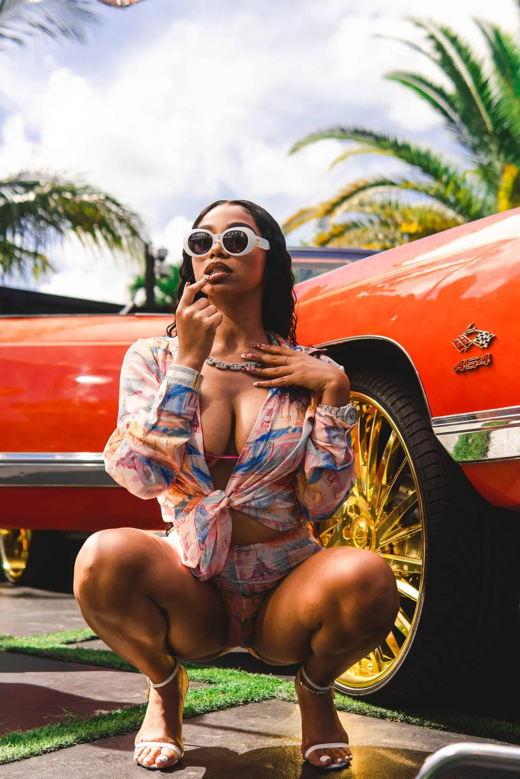 Woman in sunglasses seated beside a red car