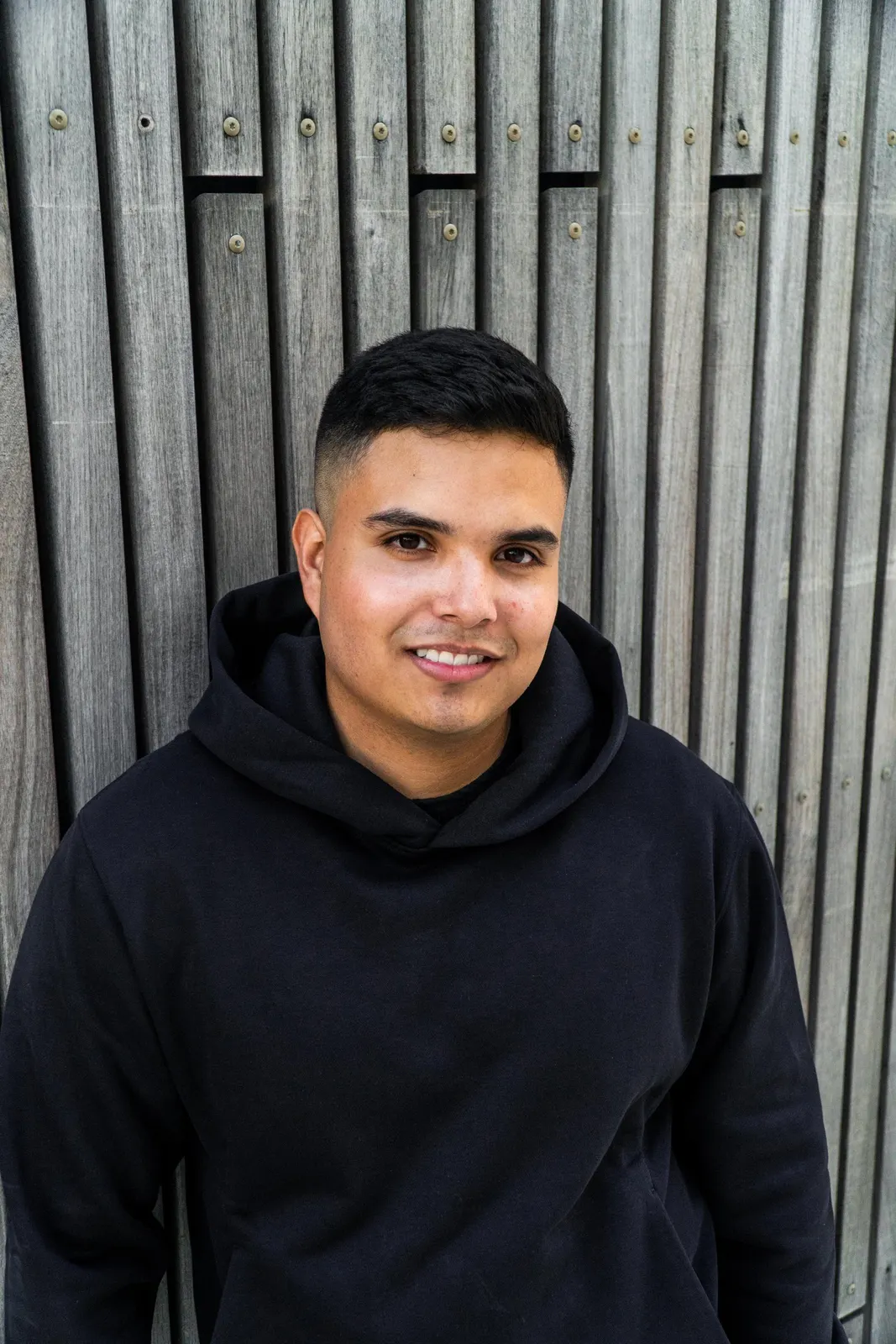 Man in a dark hoodie against a metal wall