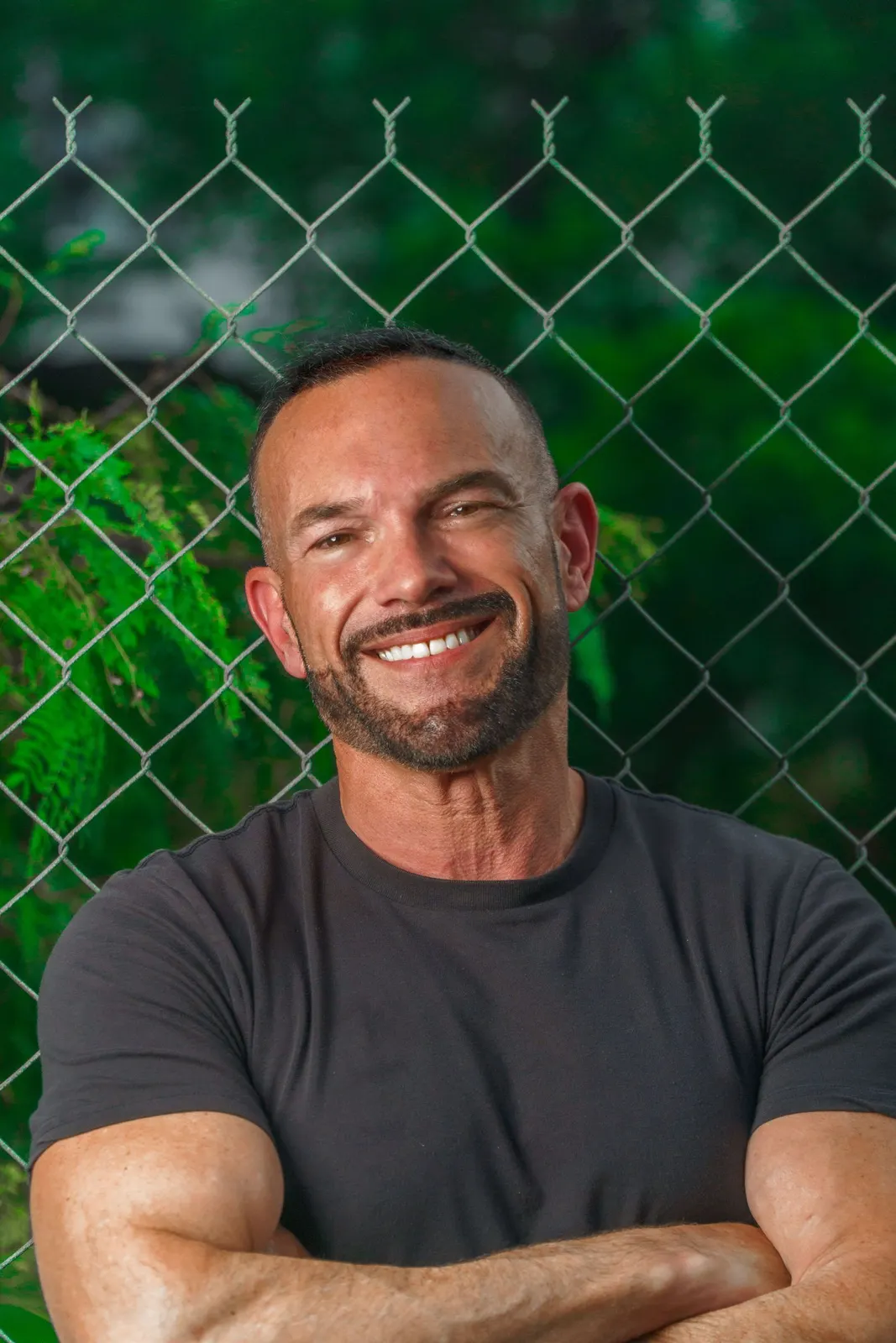 Smiling man with folded arms against a fence