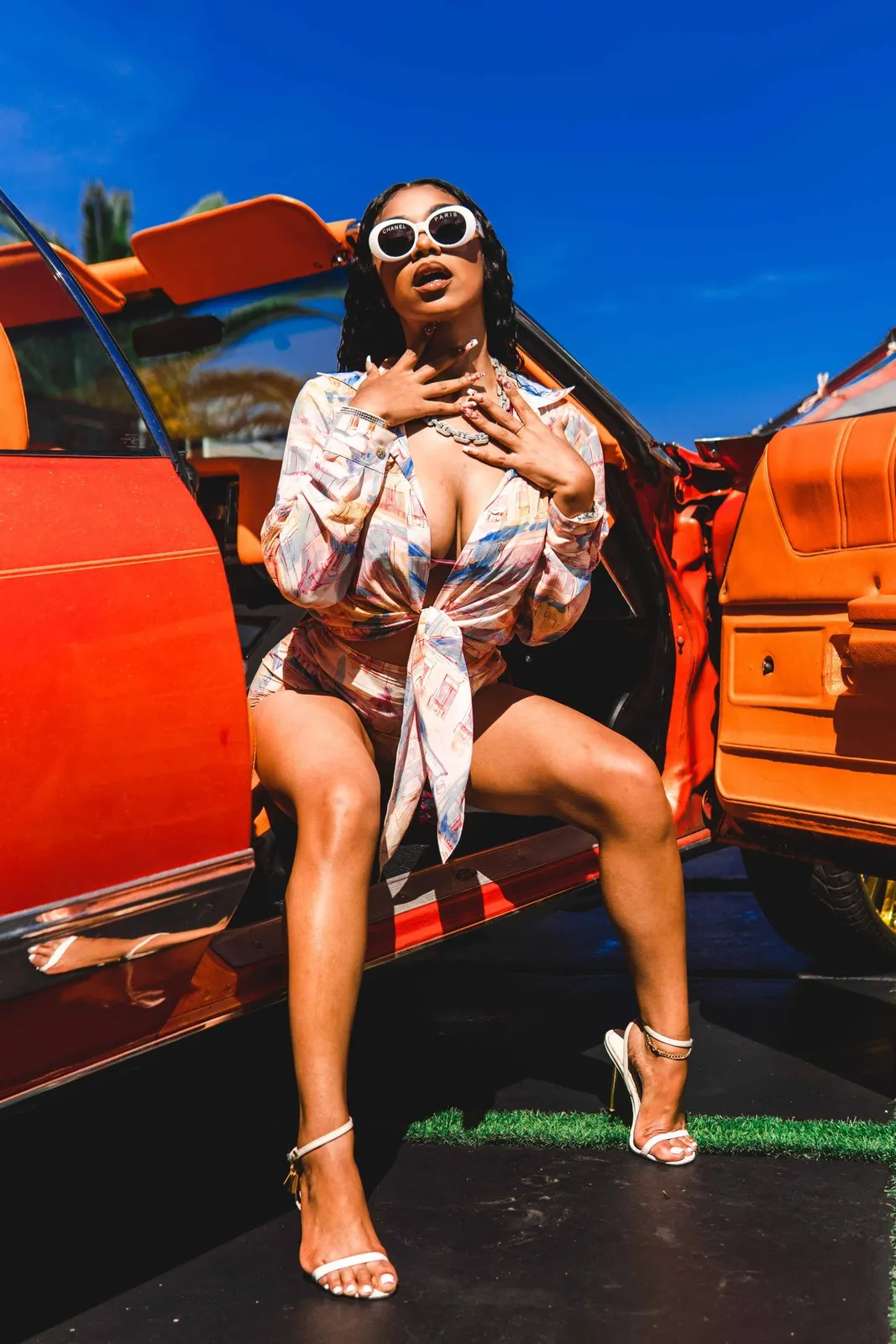 Woman in sunglasses posing beside an orange car