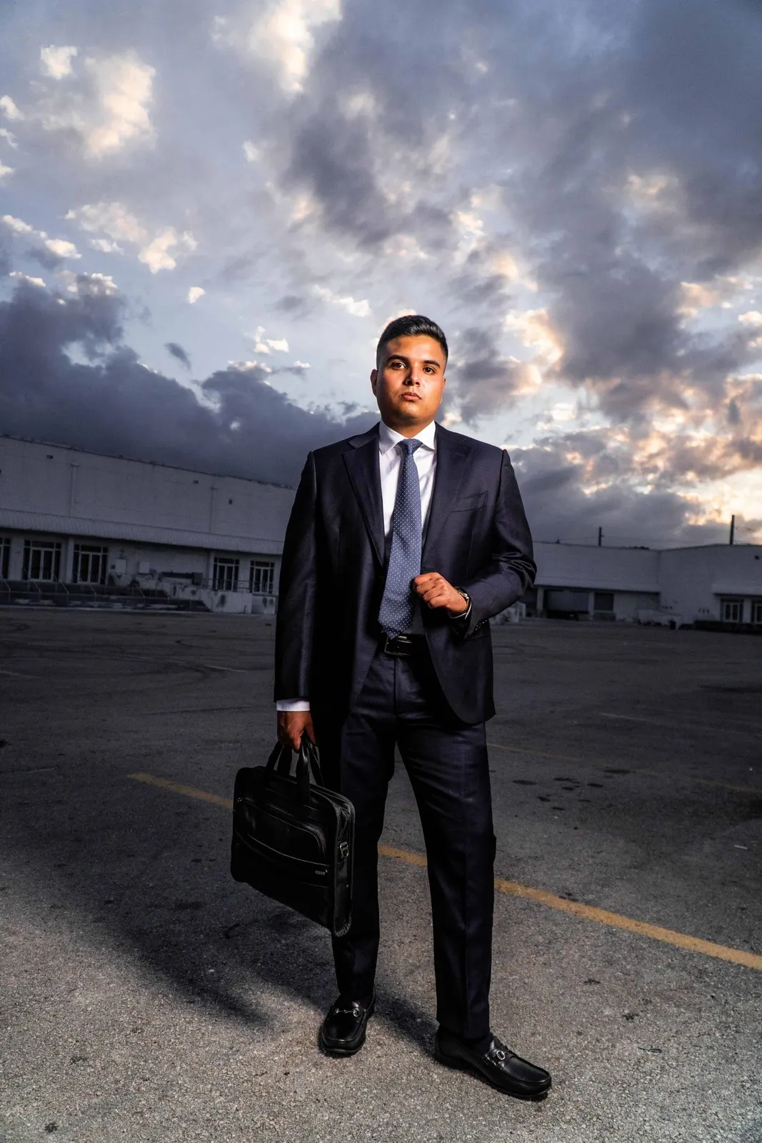 Man in a dark suit standing outdoors with a briefcase